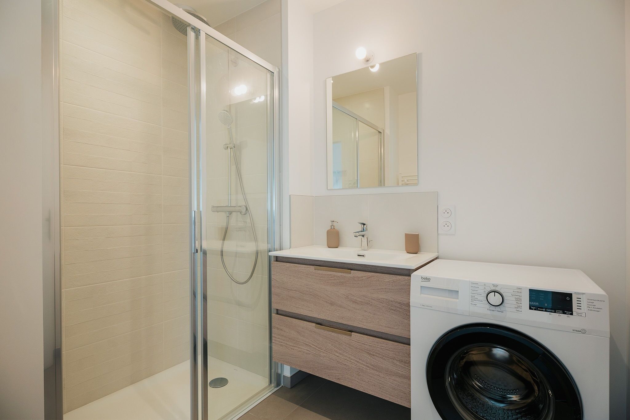 Un bagno moderno con doccia vetro, lavatrice e un mobile vanità con specchio.