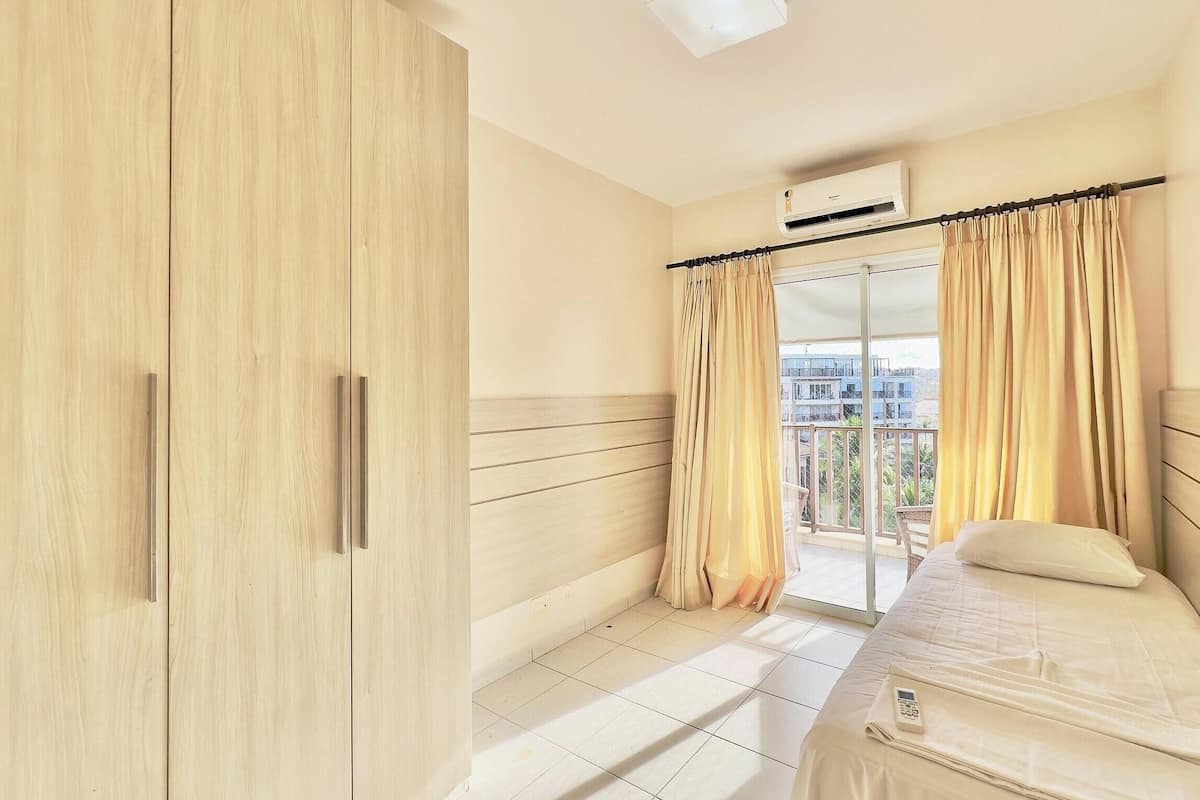Un dormitorio con cama, armario, aire acondicionado y balcón con cortinas.