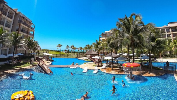 A resort pool area with multiple swimming pools, palm trees, and lounge chairs. - Beach Living Pe na Areia por Be My Guest (Aquiraz)