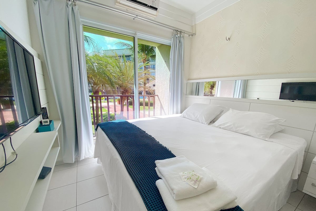 Habitación de hotel con cama, televisión y balcón con cortinas.