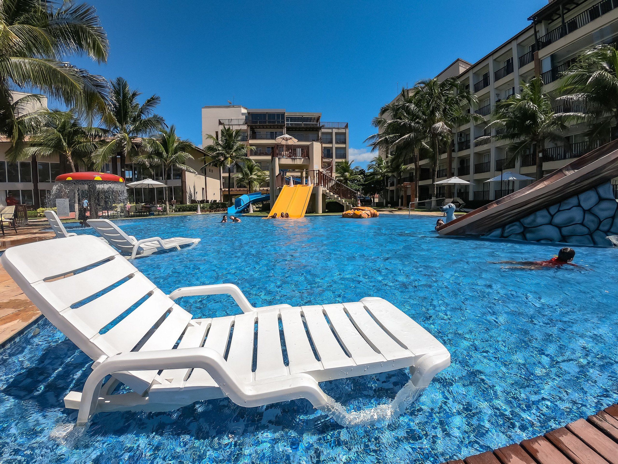 Una piscina con toboganes y sillas de descanso, rodeada de palmeras y edificios de hotel.