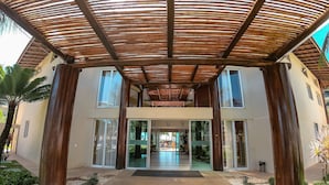 A building entrance with a wooden pergola, glass doors, and a paved pathway. - Beach Living Pe na Areia por Be My Guest (Aquiraz)