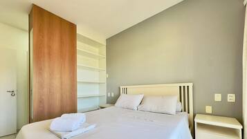 Quarto de hotel com cama, guarda-roupa de madeira e mesa de cabeceira.