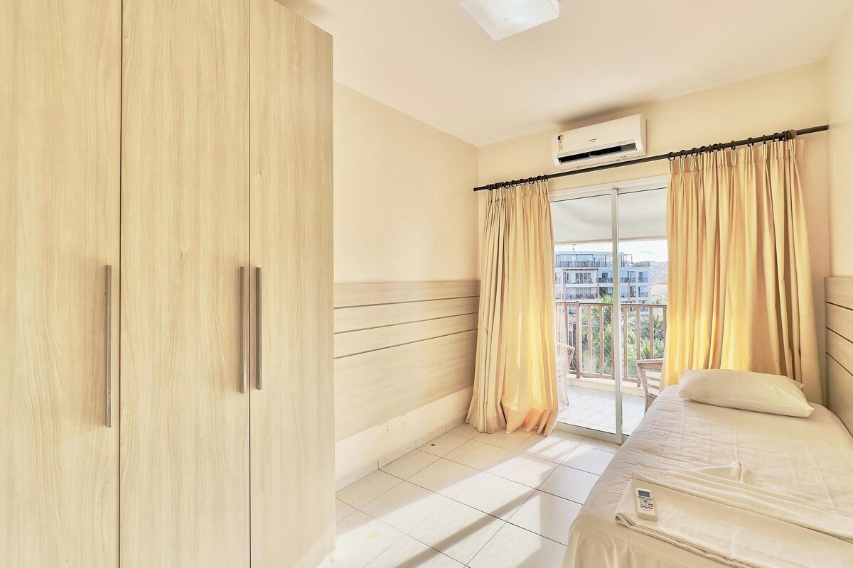 Quarto de hotel com cama, guarda-roupa, varanda com cortinas e ar condicionado.