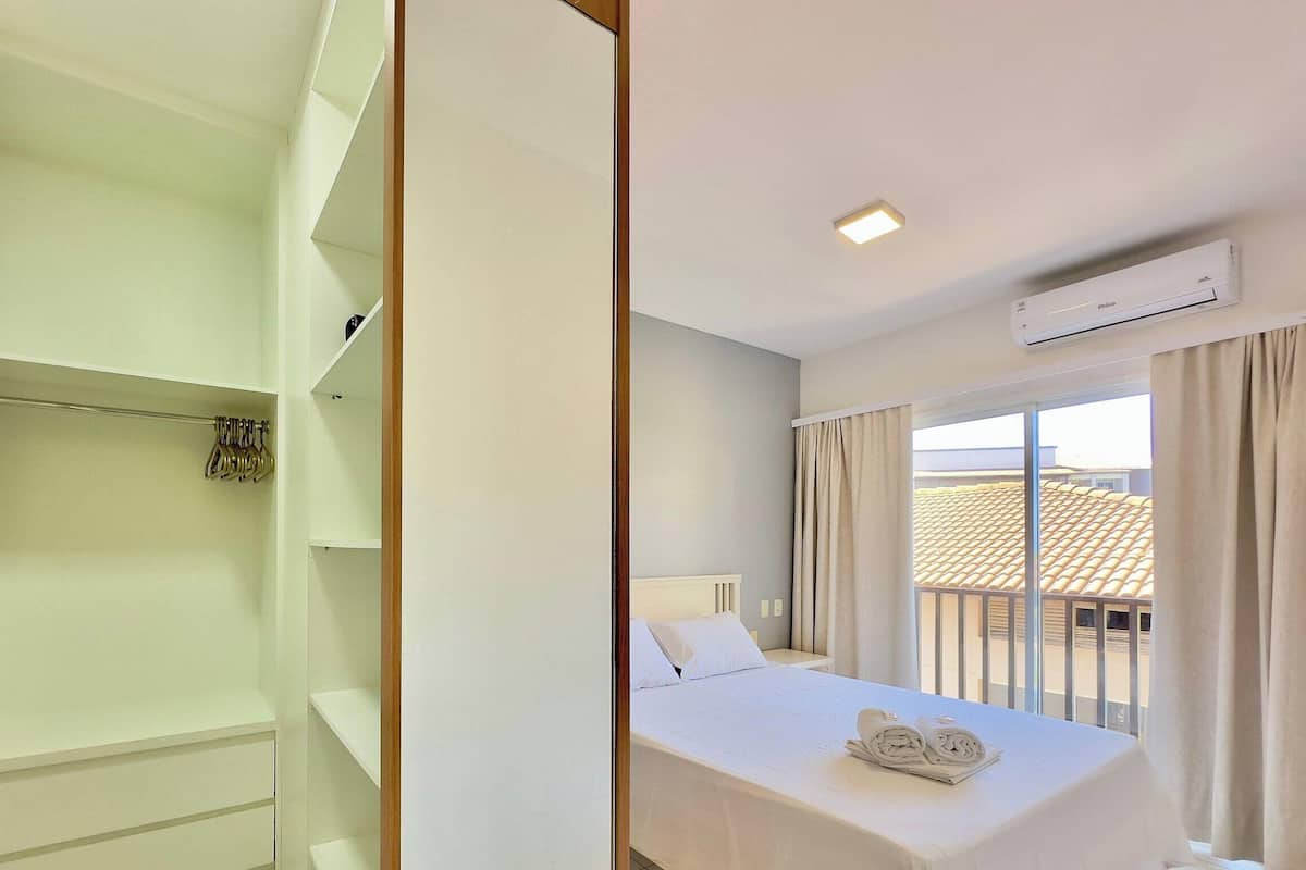 Una habitación de hotel con cama, armario, ventana con cortinas y aire acondicionado.
