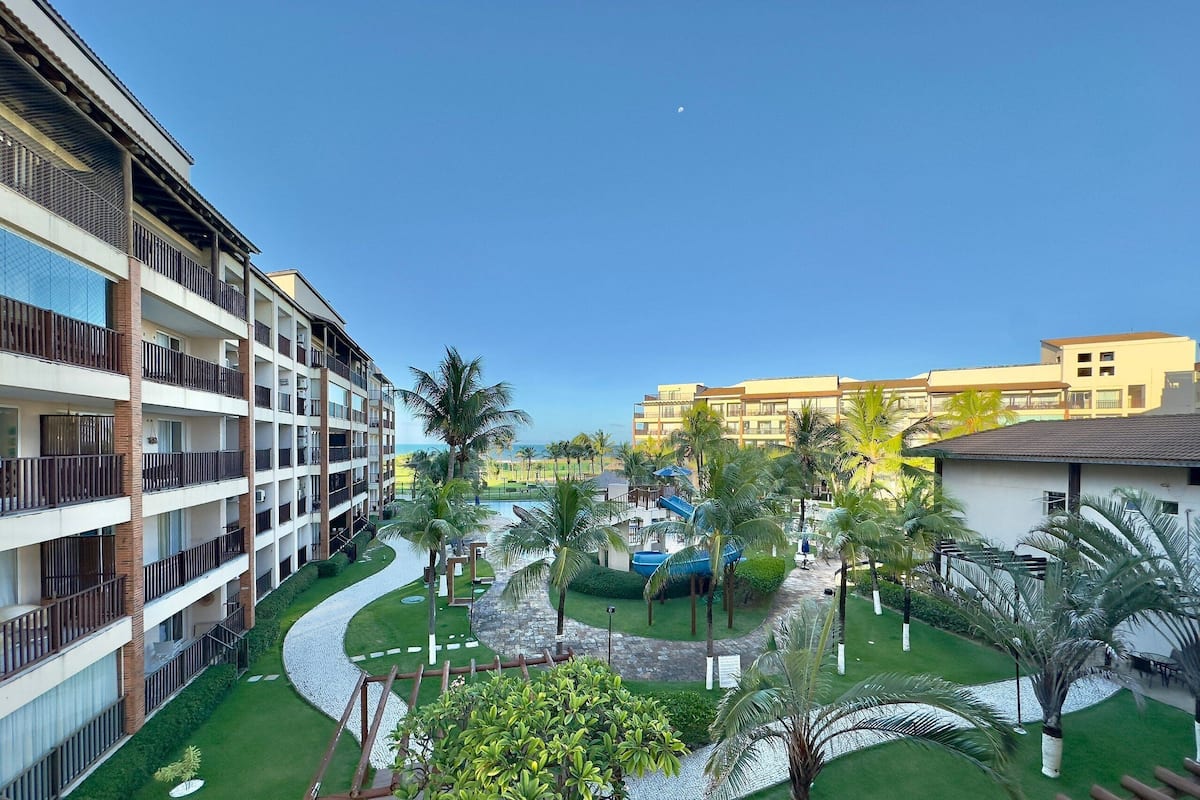 Un hotel de varios pisos con balcones, piscina y palmeras.