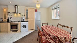 A compact kitchen with a washing machine, oven, and a dining area with a table and chairs. - Bakers Court by Guestz (Chester)