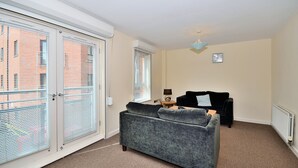 A living room with a grey sofa, a black armchair, a small wooden table with a lamp, and a ceiling fan. - Bakers Court by Guestz (Chester)