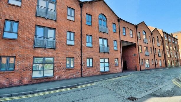 A row of red brick buildings with multiple windows and balconies, a cobblestone street, and a clear blue sky. - Bakers Court by Guestz (Chester)