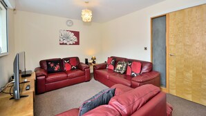 A living room with two red leather sofas, a wooden coffee table, a flat-screen TV, and a decorative light fixture. - Bakers Court by Guestz (Chester)