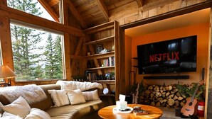 Interior acogedor de una cabaña con techo de madera, un sofá, una mesa de centro, una estantería y un televisor que muestra el logo de Netflix.