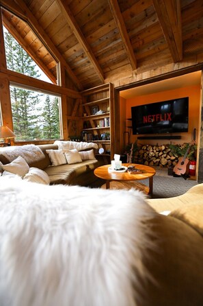 L’intérieur d’un chalet accueillant, avec un plafond en bois, un canapé, une table basse, une bibliothèque et un téléviseur affichant le logo de Netflix.
