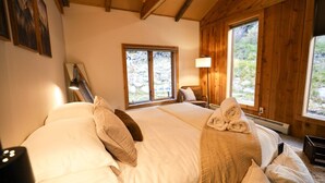 Un dormitorio de cabaña de madera con cama, almohadas, una lámpara y una ventana.