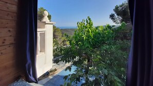 Blick durch ein Fenster mit Vorhängen, einem weißen Geländer und einem Baum im Vordergrund.