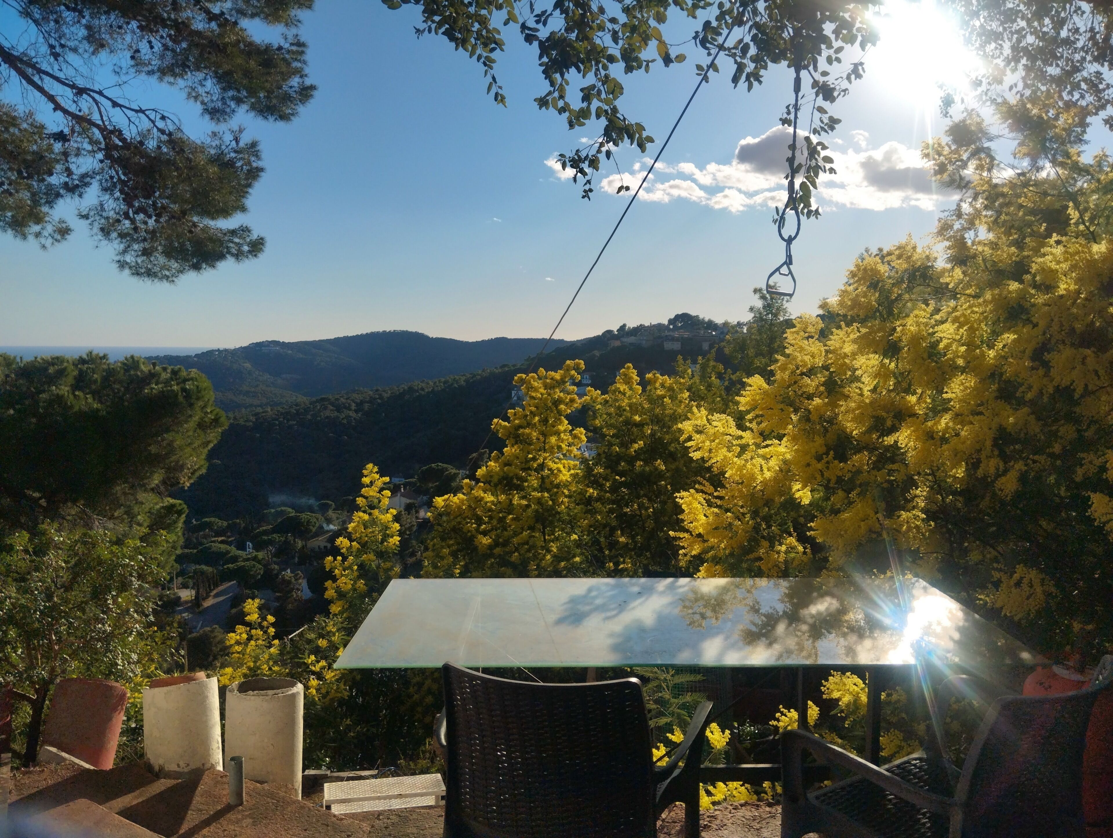 A table with chairs, a glass top, and a view of a valley with trees and hills.