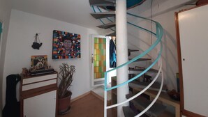 Eine Wendeltreppe mit einer weißen Säule und türkisblauen Geländern, ein Blumentopf, ein farbenfrohes abstraktes Gemälde und eine Tür zu einem anderen Raum.