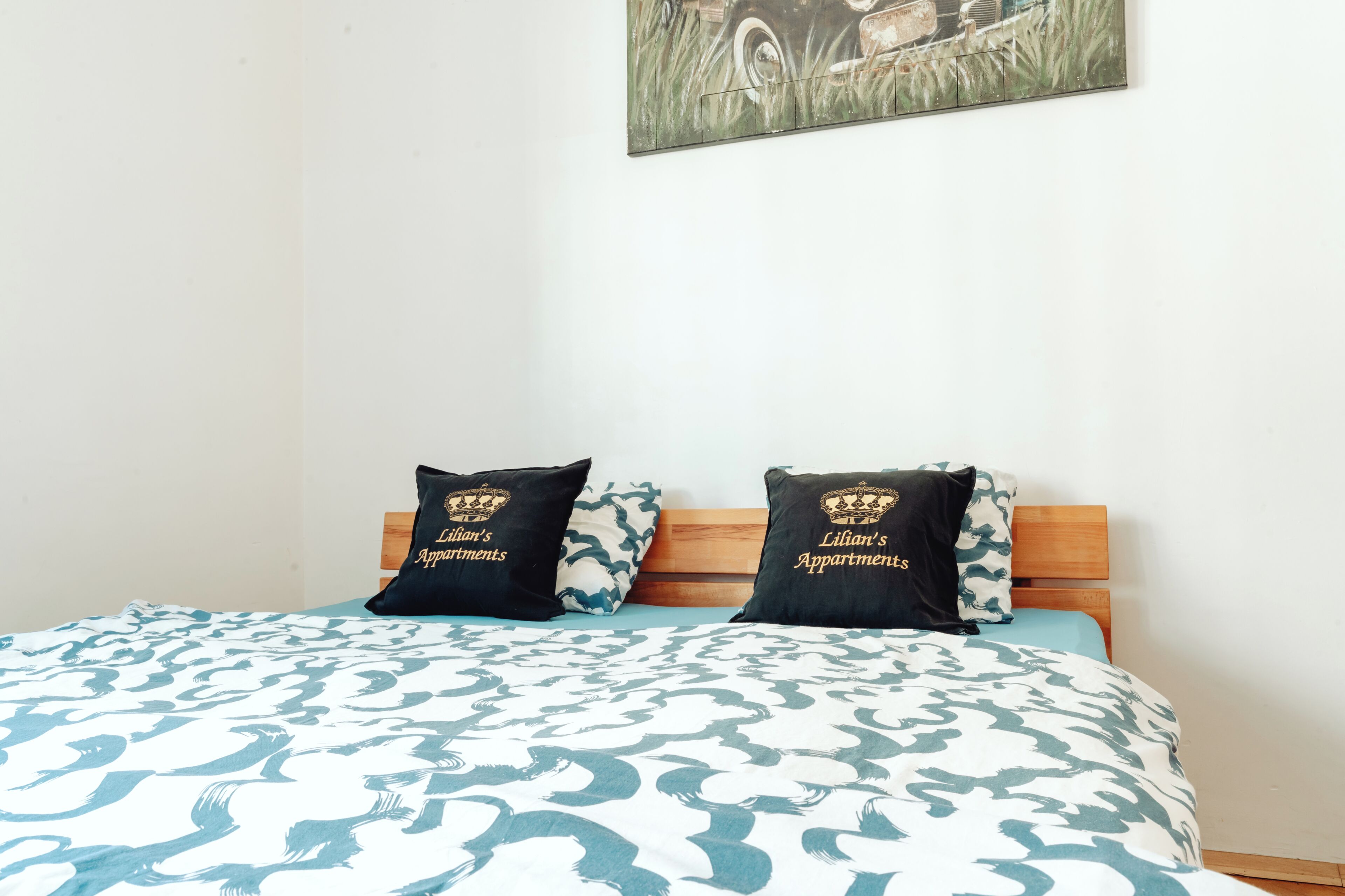 A bed with a patterned bedspread, two pillows with text, and a painting on the wall.
