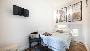 Een slaapkamer met een bed, een stoel, een televisie en kunst aan de muur.