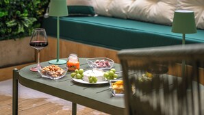 Een terras met een gedekte tafel voor een maaltijd, omgeven door weelderige begroeiing en een bank met kussens.