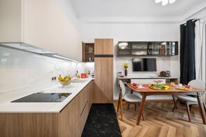 A modern kitchen with a built-in oven, a dining table with chairs, and a black marble countertop. - Luxury apartment in the center of town (Nice)