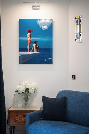 A room with a blue sofa, a painting of two people by the sea, a vase with flowers, and a small table with a decorative item. - Luxury apartment in the center of town (Nice)
