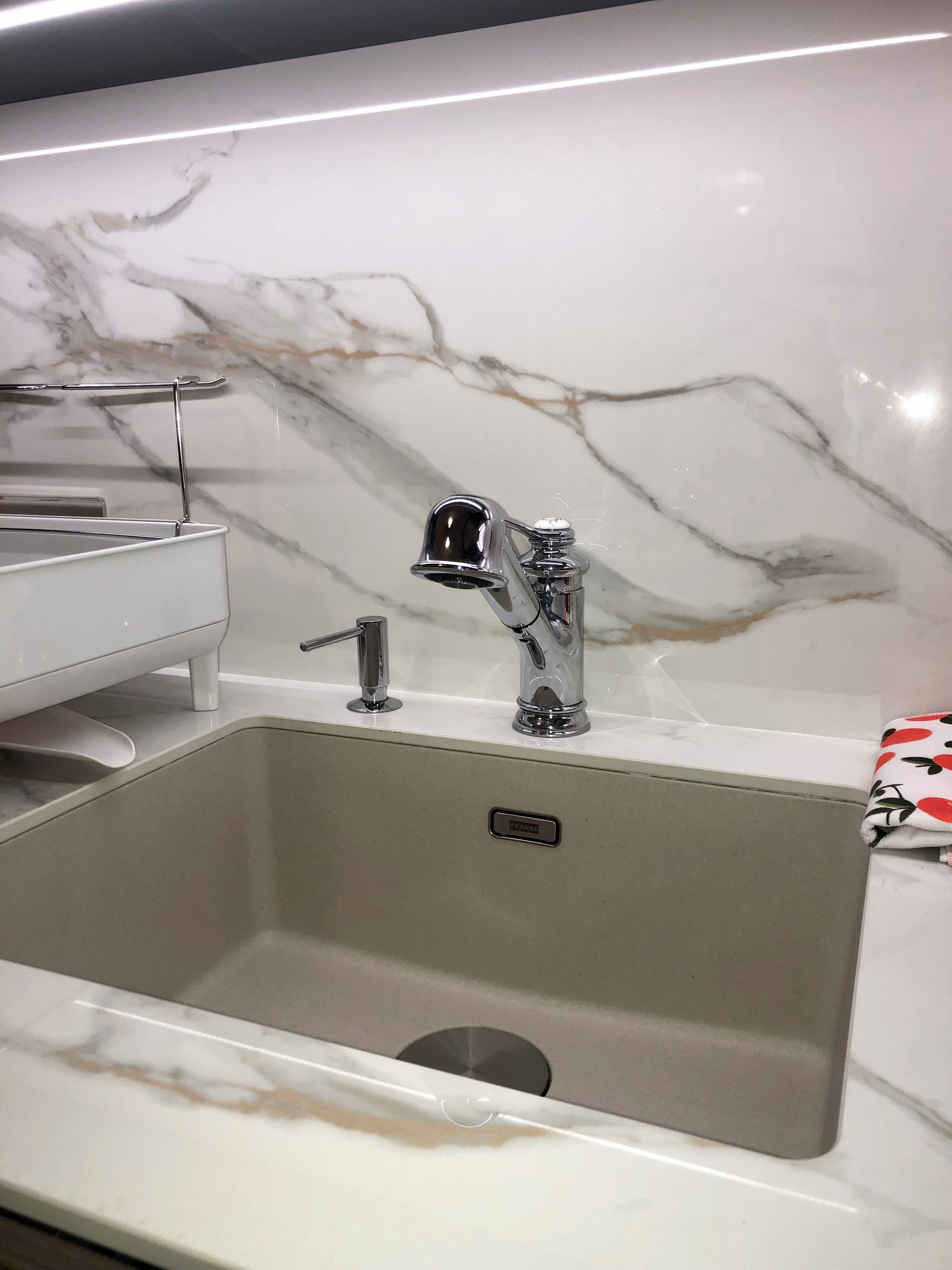 En modern köksdiskho med en blandare, en inbyggd soptunna och en väggbeklädnad av marmor.