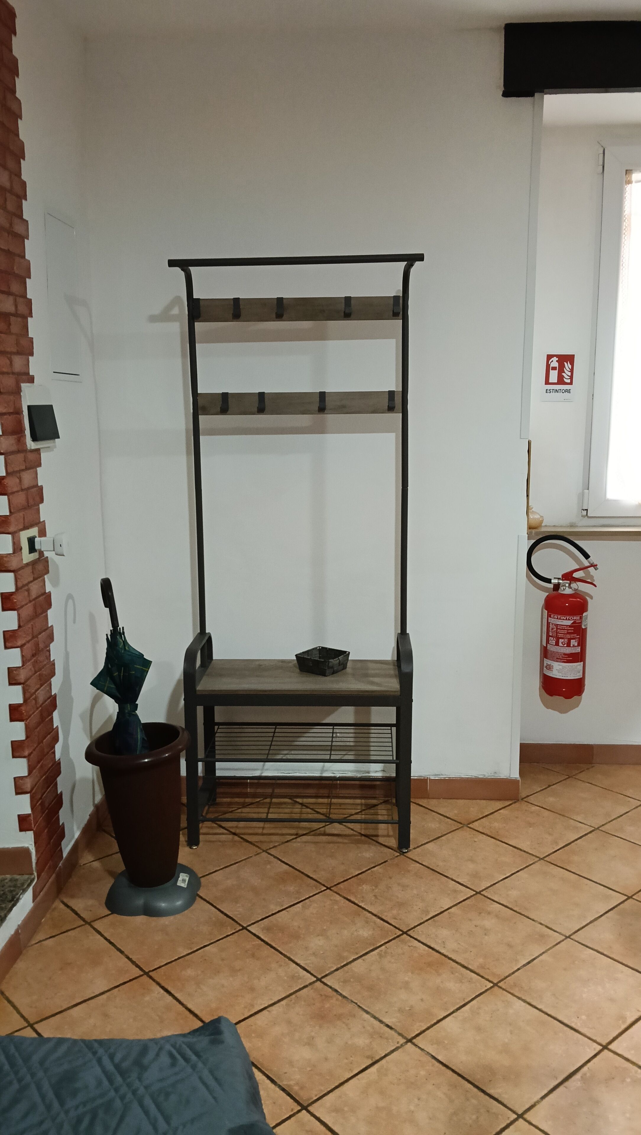 Una stanza con una rastrelliera metallica, una pianta in vaso, un estintore e un pavimento piastrellato.