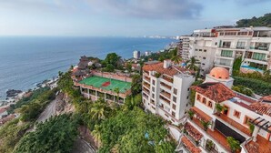 Un hotel costero con varias edificaciones, una cancha de tenis y vista al mar.