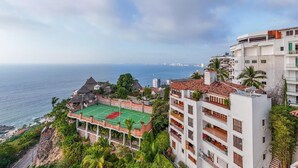 Un hotel frente al mar con cancha de tenis, vistas al océano y un edificio de varios pisos con balcones.