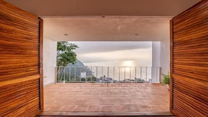 Un balcón abierto con vistas a un paisaje urbano y un árbol.