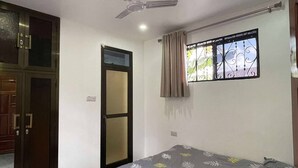 Un dormitorio con cama, ventilador de techo, ventana con cortinas y puerta.