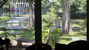 Vista attraverso una finestra su un giardino con uno stagno, un'amaca e un recinto bianco.