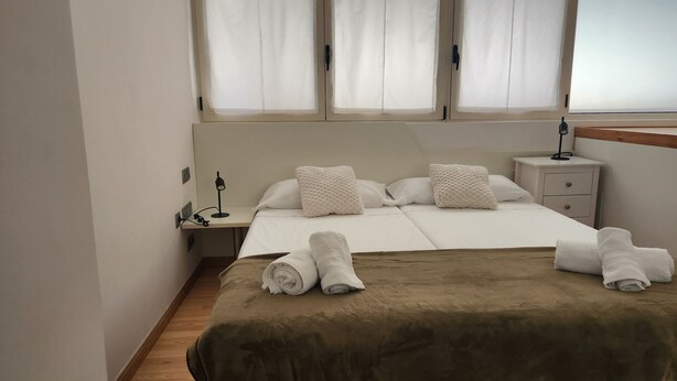 A hotel room with a bed, two pillows, a bedside table with a lamp, a nightstand, and a window with curtains. - La Concha Apartment (Donostia / San Sebastián)