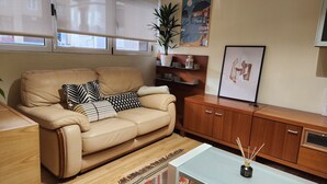 A living room with a beige sofa, patterned cushions, a wooden cabinet, a glass coffee table, a potted plant, and a framed picture on the wall. - La Concha Apartment (Donostia / San Sebastián)