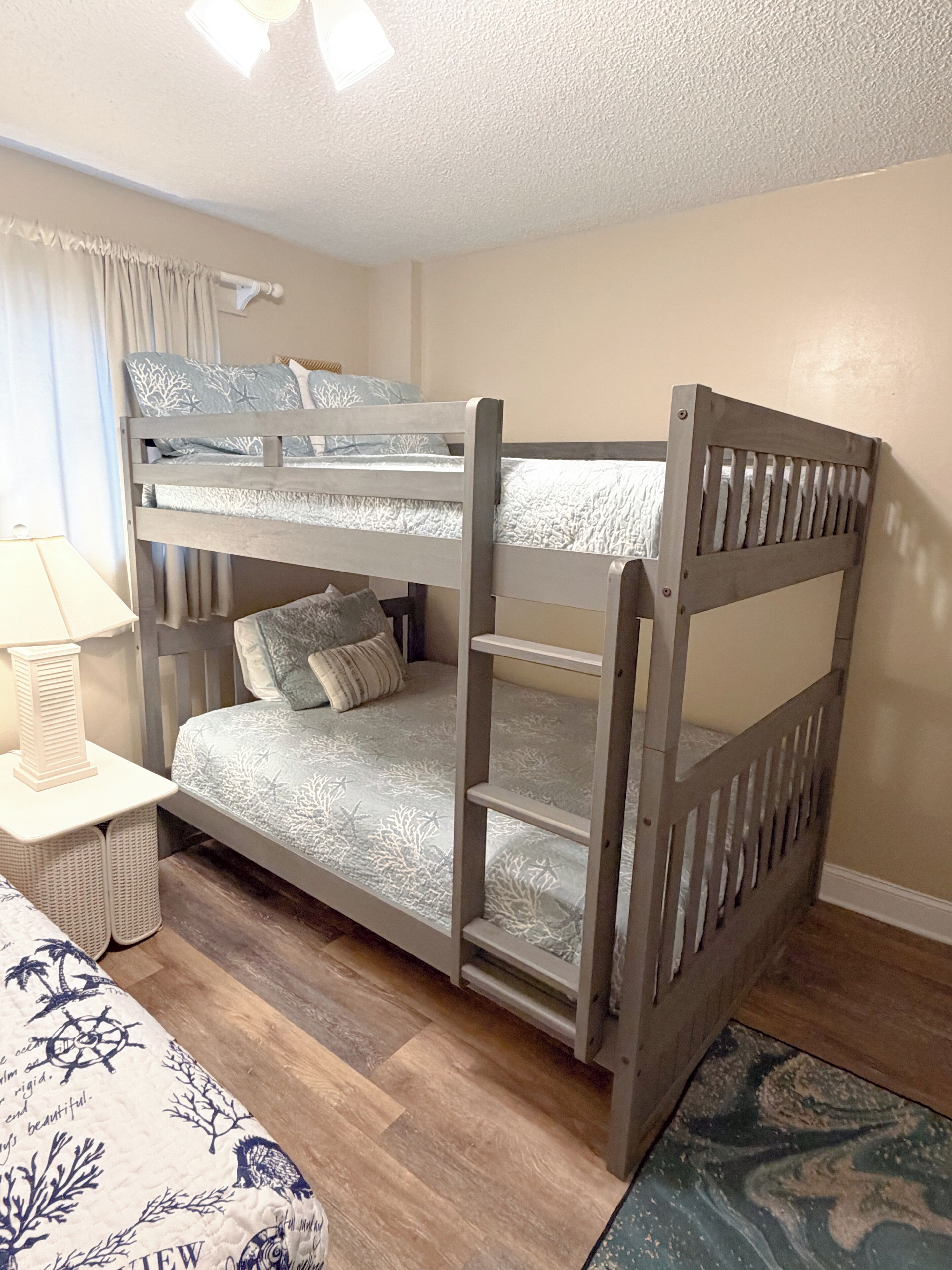 A bunk bed with a ladder, a bedside table with a lamp, and a patterned bedspread.