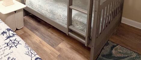 A bunk bed with a ladder, a bedside table with a lamp, and a patterned bedspread.