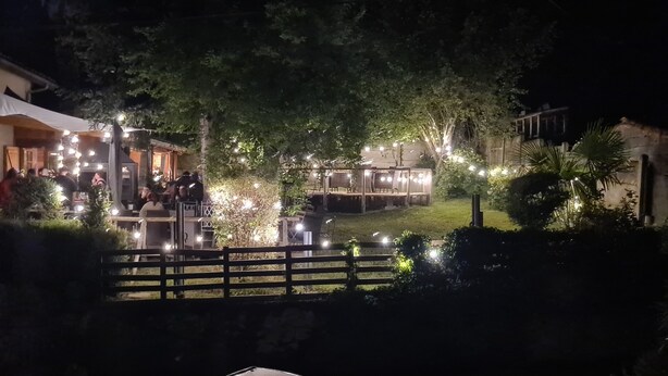 An outdoor dining area with string lights, a wooden fence, and a building in the background.