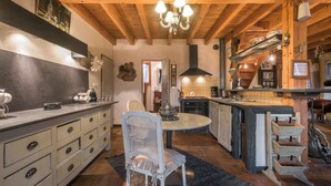 A kitchen with wooden beams, a chandelier, a dining table, and a chair.