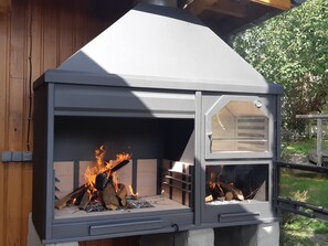 En vedeldad kamin med en skorsten, omgiven av ett trästaket och grönska.