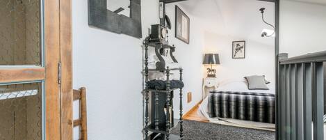 A bedroom with a bed, a bedside table, a lamp, a mirror, and a black and white patterned rug.