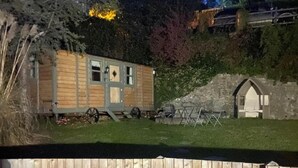 A wooden cabin with a small attached shed, a fenced yard, and a stone wall. - Riverside Retreats Shepherds Hut in Newtown Wales (Newtown)