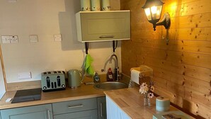 A kitchen with a toaster, kettle, sink, and a wall-mounted light fixture. - Riverside Retreats Shepherds Hut in Newtown Wales (Newtown)