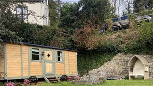 A small wooden cabin with a porch, a stone wall, and a shed. - Riverside Retreats Shepherds Hut in Newtown Wales (Newtown)