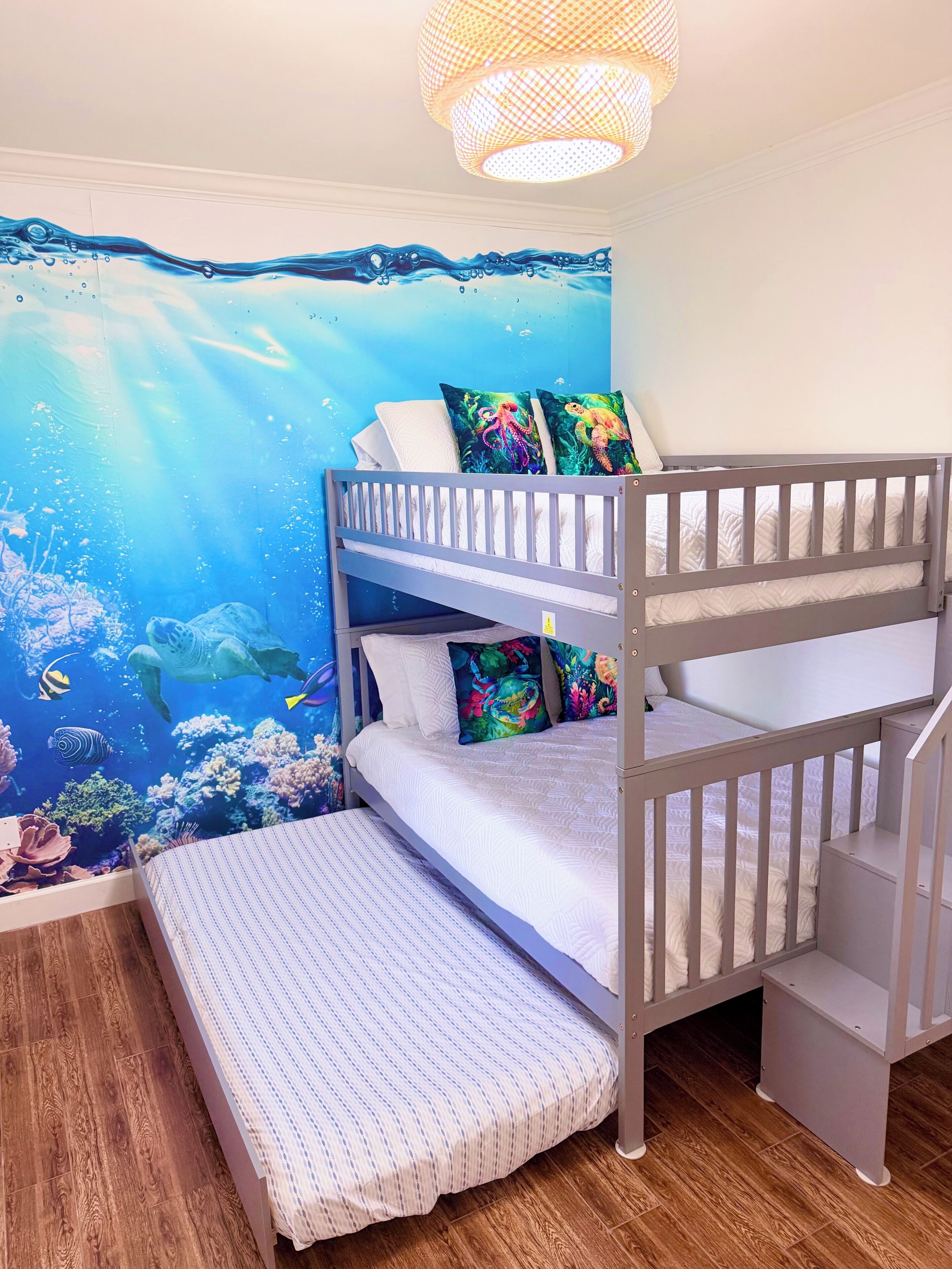 Ein Etagenbett mit einer farbenfrohen Wandmalerei einer Unterwasserlandschaft, Holzboden und einer Pendelleuchte.