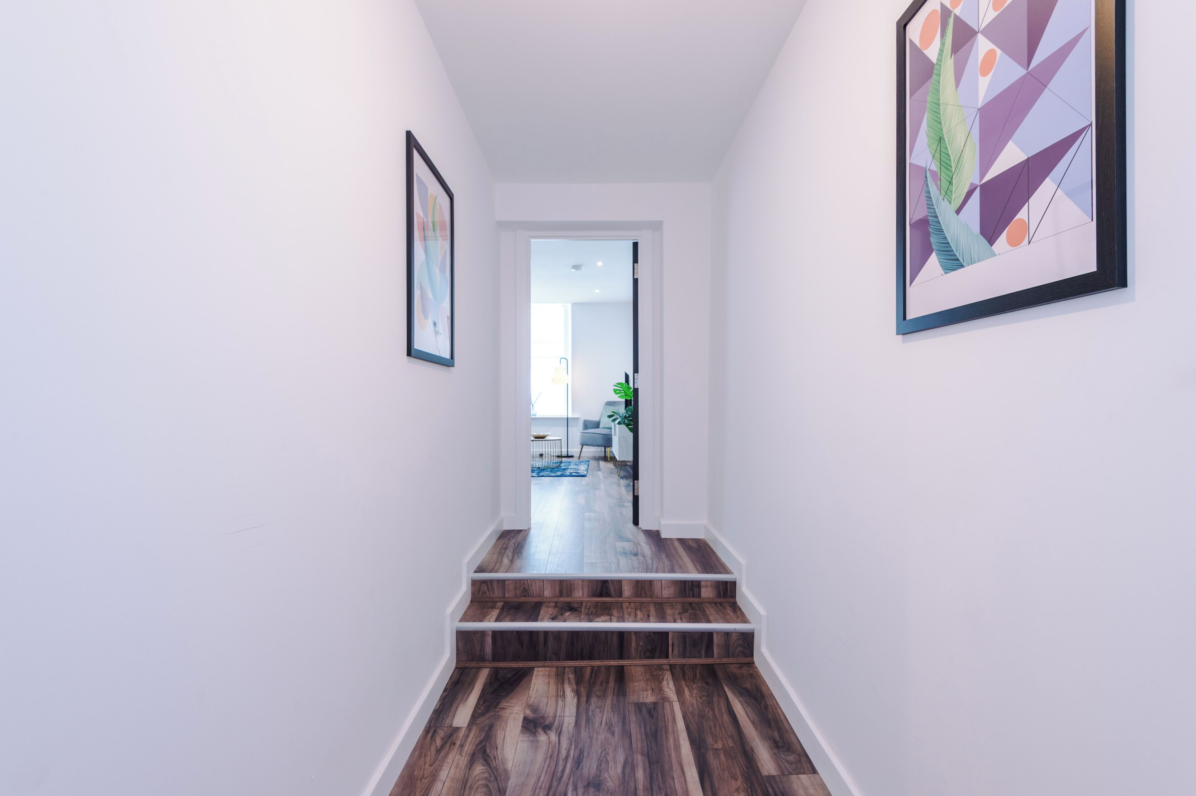 A hallway with wooden stairs, white walls, and two framed artworks.