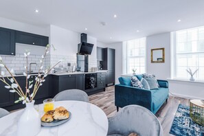 A modern kitchen with dark cabinets, a white countertop, and a dining area with a round table and chairs. - Binding House by Guestz (Hull)
