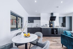 A modern kitchen with dark cabinets, a built-in oven, and a dining area with a round table and chairs. - Binding House by Guestz (Hull)