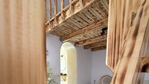 Een kamer met een hoog plafond, houten balken, een betegelde vloer, een bank en een decoratief kussen.