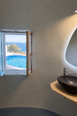 A bathroom with a window, a sink, and a view of a pool and ocean. - LOFT KAVES POOL AND BAR SUITES - ΜΟΝΑΔΙΚΟ ΘΟΛΩΤΟ ΠΑΤΑΡΙ ΜΕ ΚΥΚΛΑΔΙΤΙΚΗ ΑΙΣΘΗΤΙΚΗ (PYRGOS KALLISTIS, THIRA)