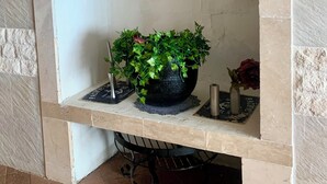 Uma lareira com uma prateleira que contém uma planta em vaso, uma vela e um vaso com uma flor.